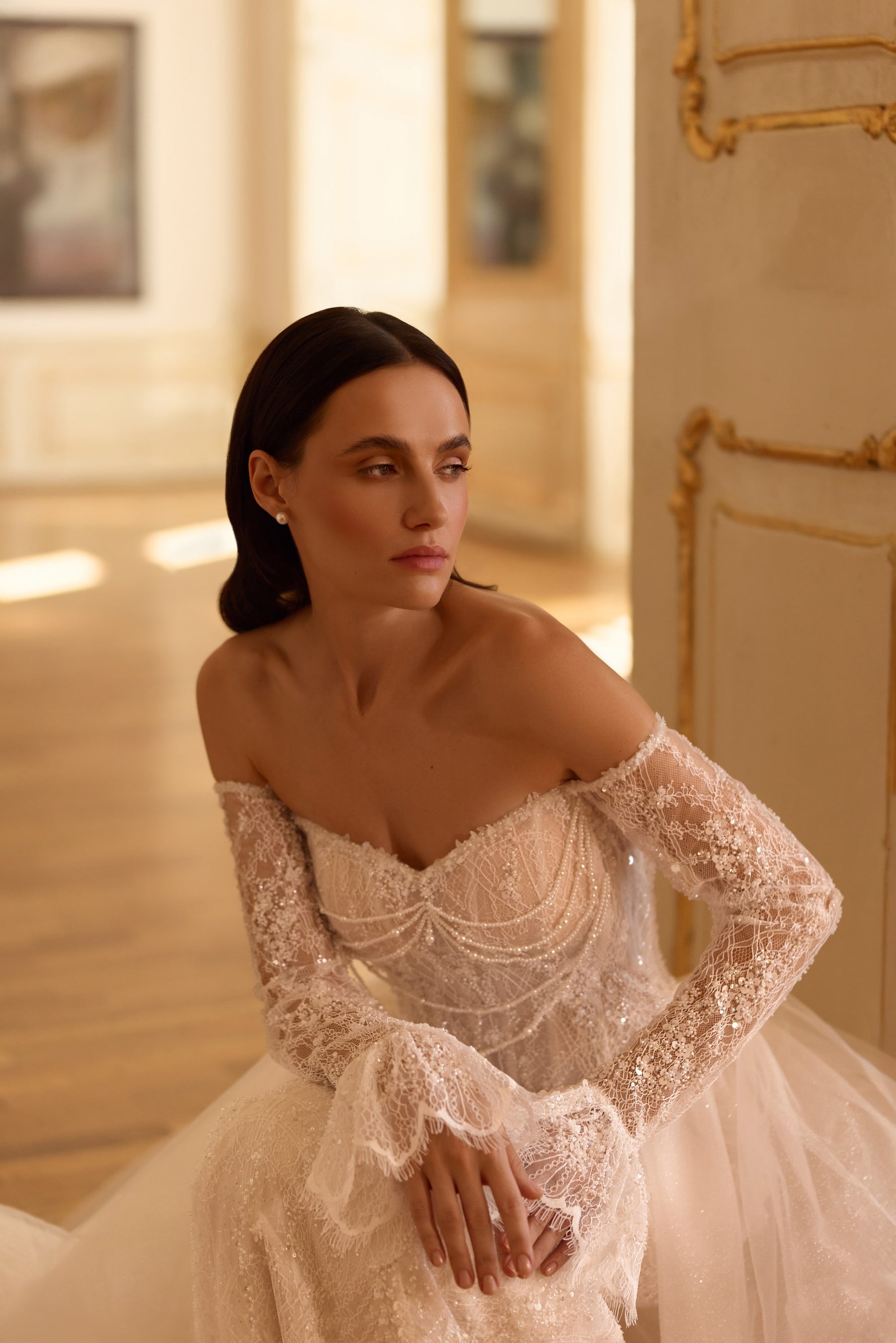 Close-up of an ivory wedding dress bodice with an off-shoulder neckline, long lace sleeves, and draped beadwork