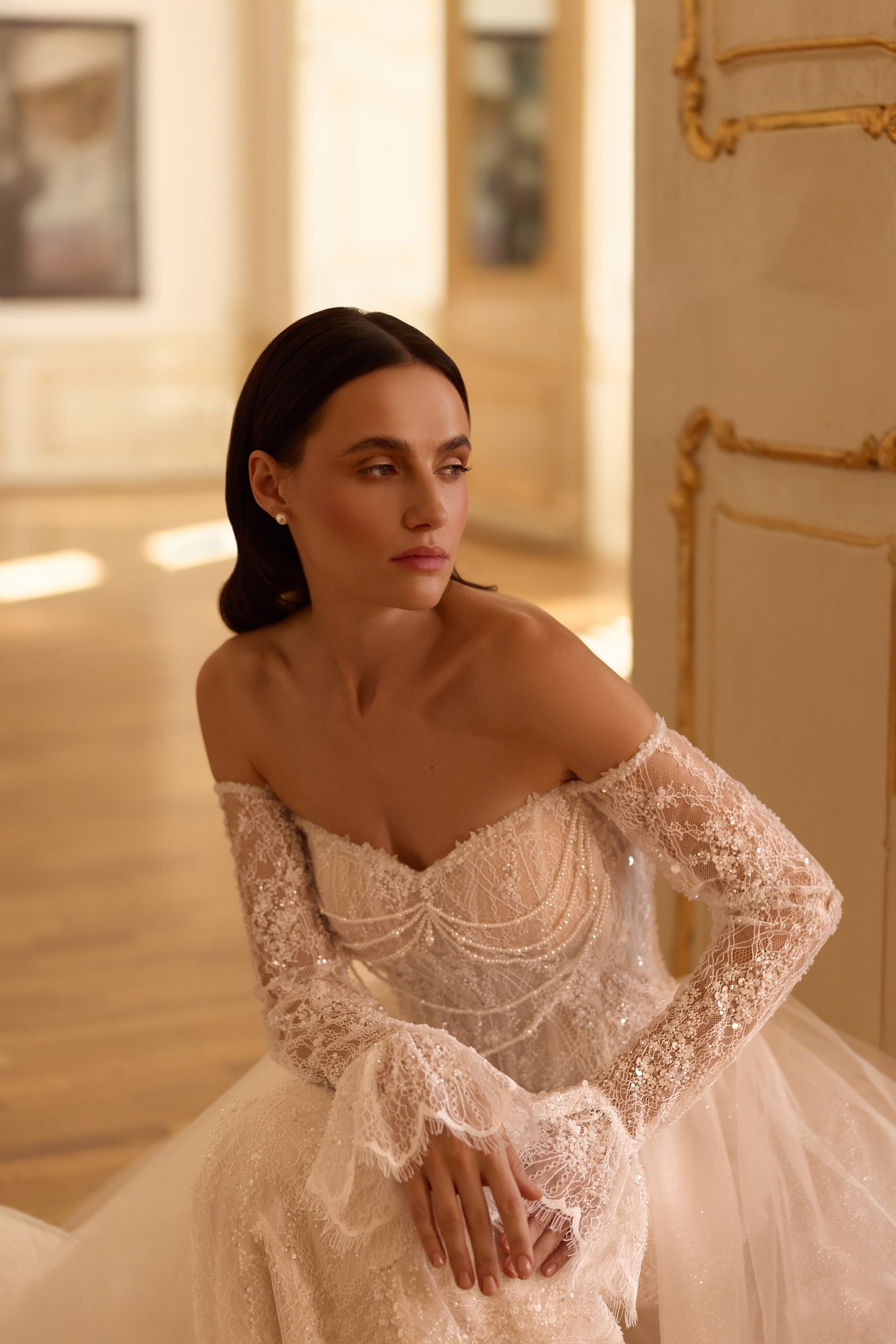 Close-up of an ivory wedding dress bodice with an off-shoulder neckline, long lace sleeves, and draped beadwork