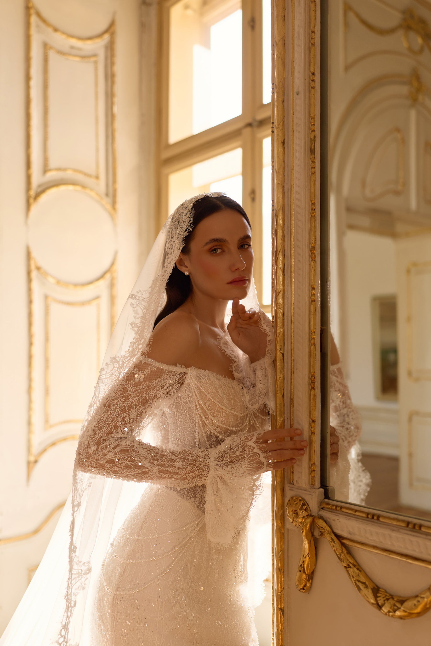 Ivory wedding dress with an off-shoulder lace neckline, long sleeves, shimmering embellishment, and fitted silhouette