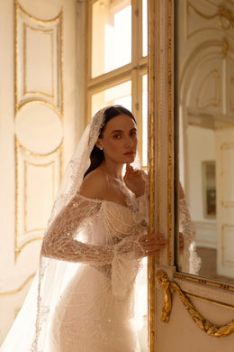Ivory wedding dress with an off-shoulder lace neckline, long sleeves, shimmering embellishment, and fitted silhouette