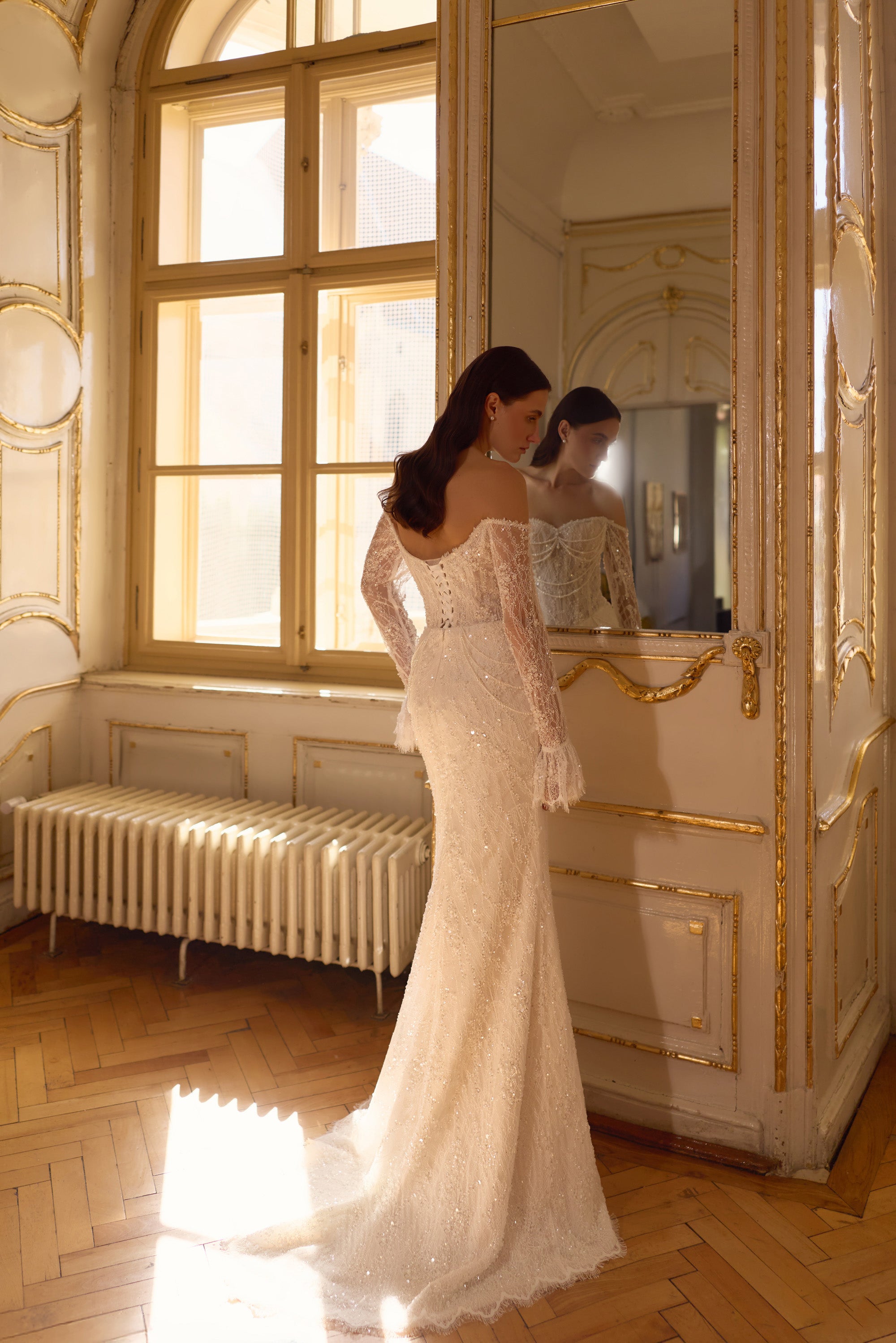 Fitted ivory mermaid wedding dress with long lace sleeves, sparkling details, and a sweeping train shown from behind