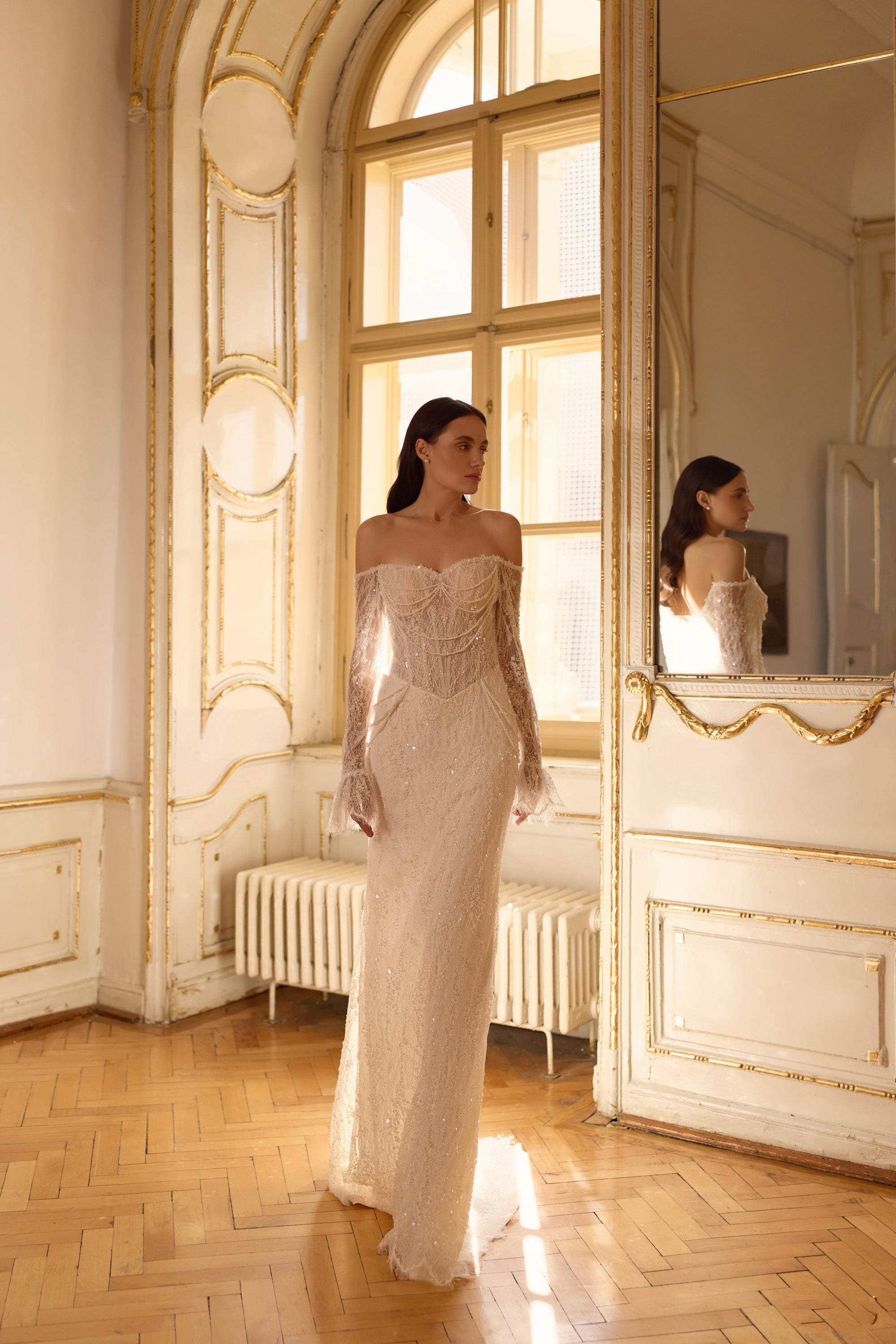 Ivory wedding dress with a straight off-shoulder neckline, long lace sleeves, fitted mermaid skirt, and glittering finish