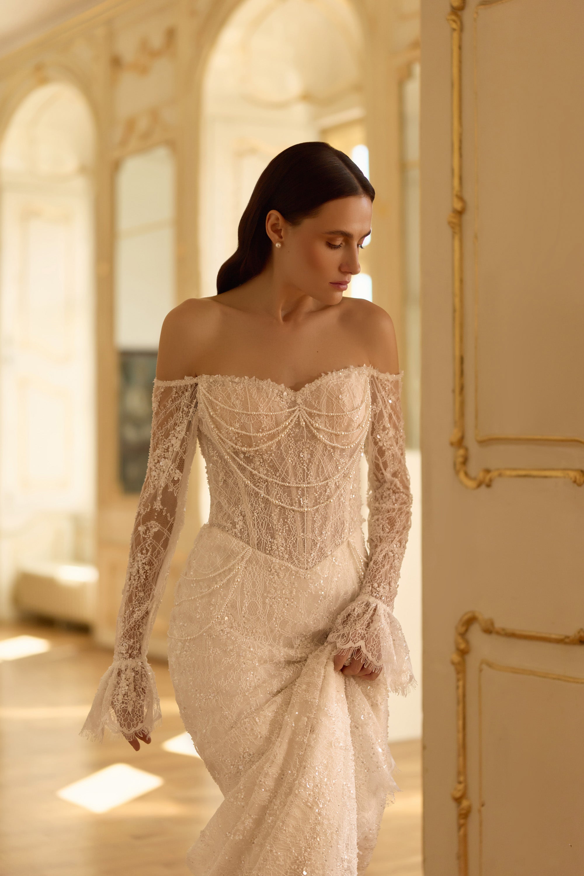Detailed ivory wedding dress bodice with draped beadwork, an off-shoulder neckline, lace sleeves, and fitted skirt