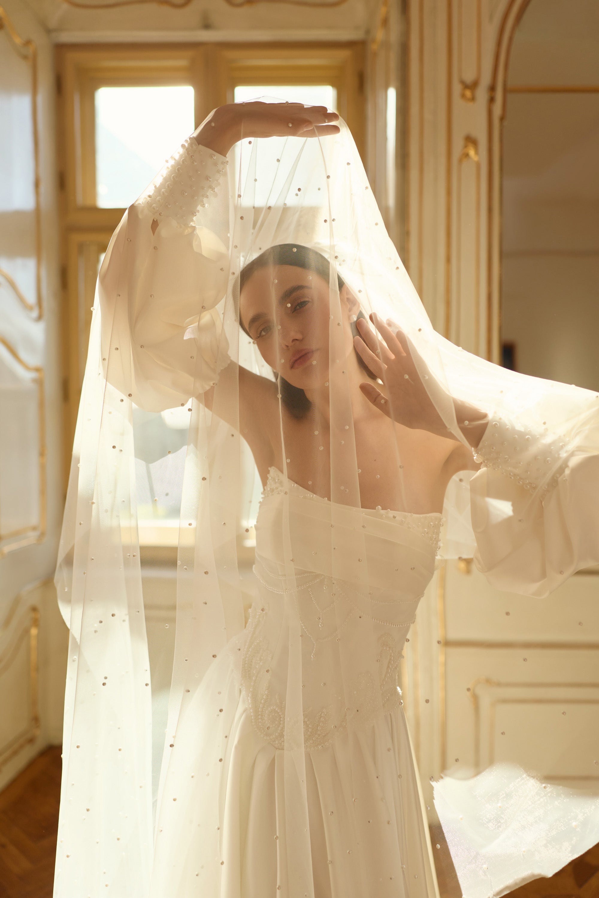 Ivory wedding dress with voluminous puff sleeves beneath a sheer, pearl-dotted veil