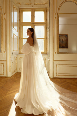Side view of an ivory wedding dress with puff sleeves, a long train, and a sheer dotted veil