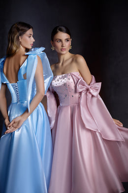 Pink A-line evening dress with a strapless embellished bodice and oversized bow drapes, beside a blue lace-up back