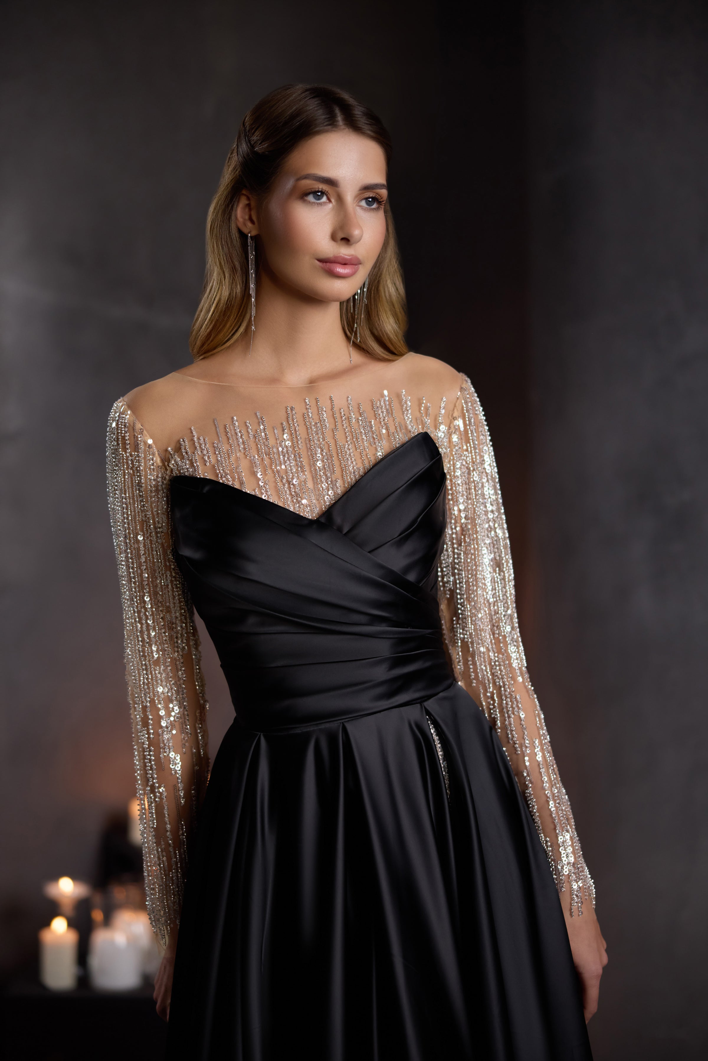 Black evening dress with a draped bodice, sheer long beaded sleeves, and flowing skirt