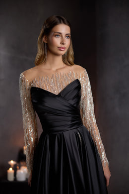 Black evening dress with a draped bodice, sheer long beaded sleeves, and flowing skirt