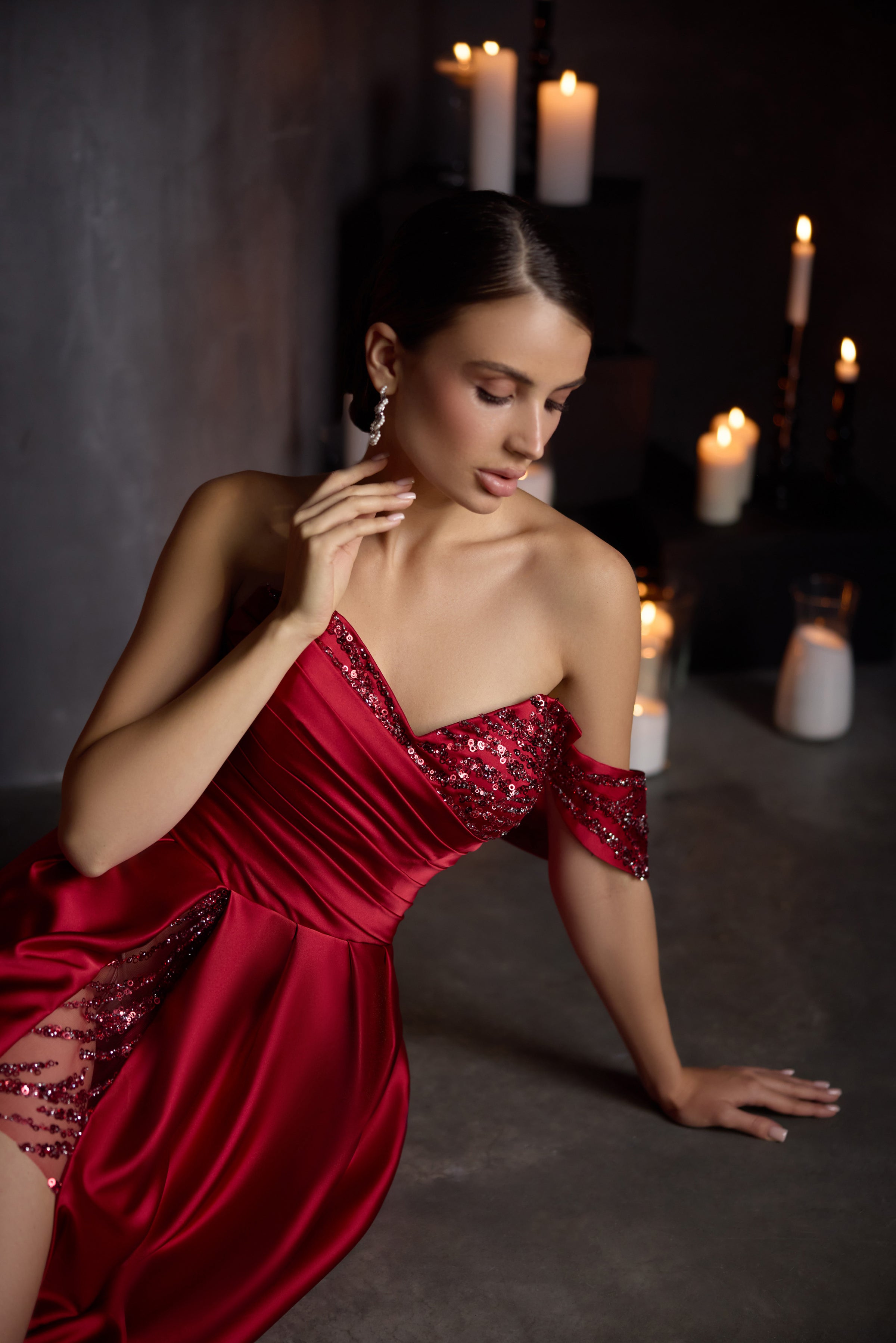 Close-up of a red evening dress with a sequined shoulder drape, ruched bodice, and embellished thigh-high slit