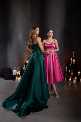 Open-back emerald green evening dress with a long flowing train beside a fuchsia pink A-line dress