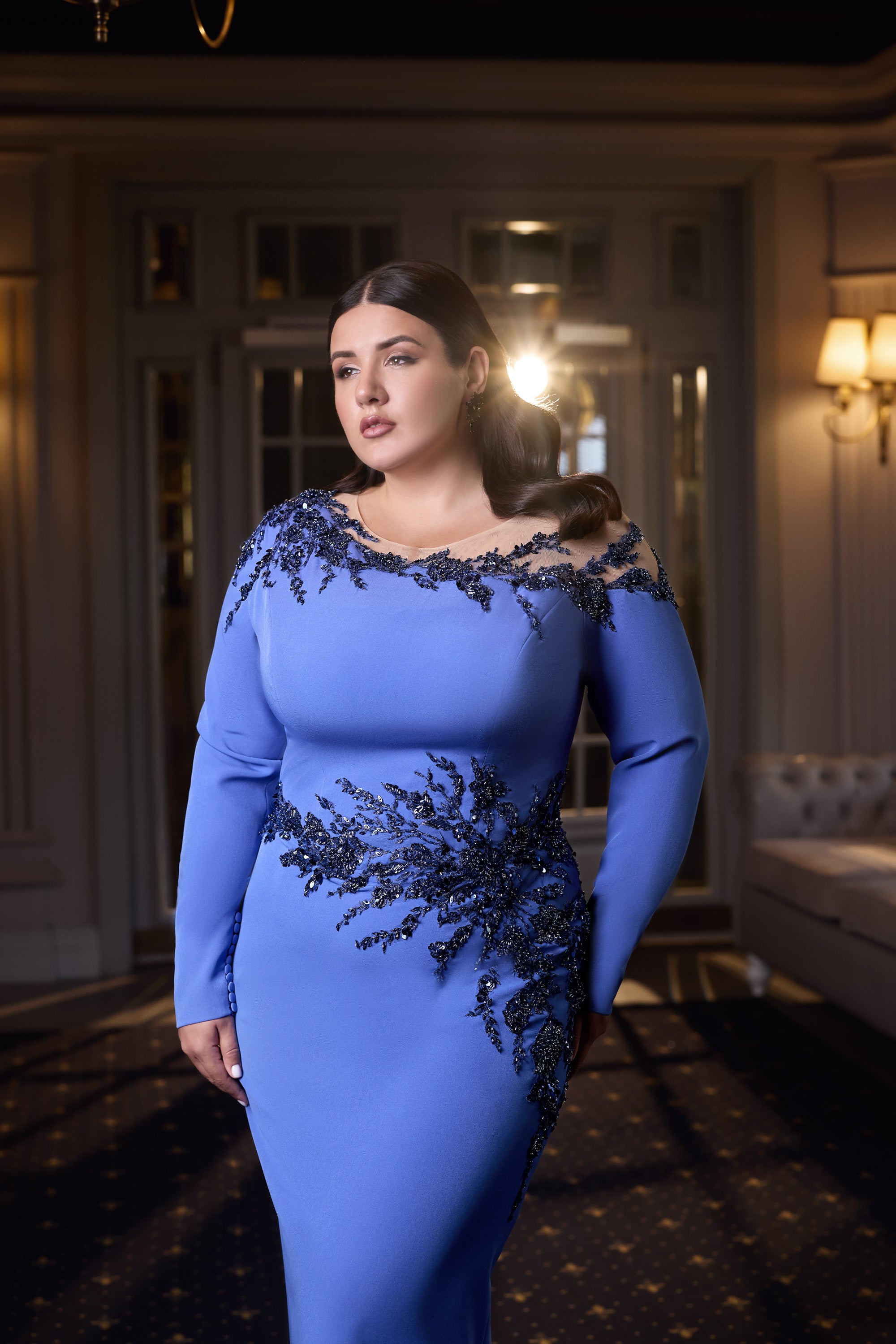 Fitted blue evening dress with long sleeves, an off-shoulder neckline, and dark floral beadwork