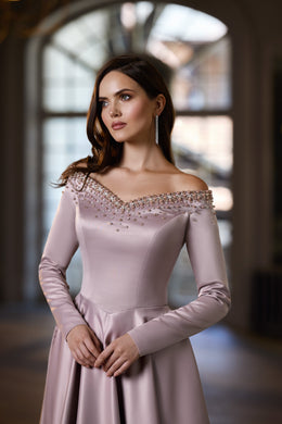 Close-up of a blush evening dress with an off-the-shoulder beaded neckline, long sleeves, and fitted bodice