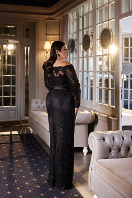Back view of a black floor-length evening dress with a lace upper back, sheer sleeves, and fitted silhouette