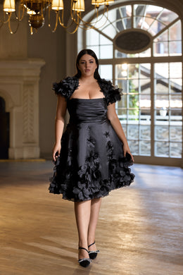 Black knee-length evening dress with a ruched bodice, floral off-shoulder sleeves, and textured appliqués