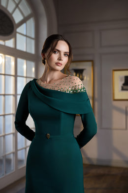 Close-up of a teal evening dress with a draped off-shoulder neckline, beaded sheer yoke, and jeweled waist button