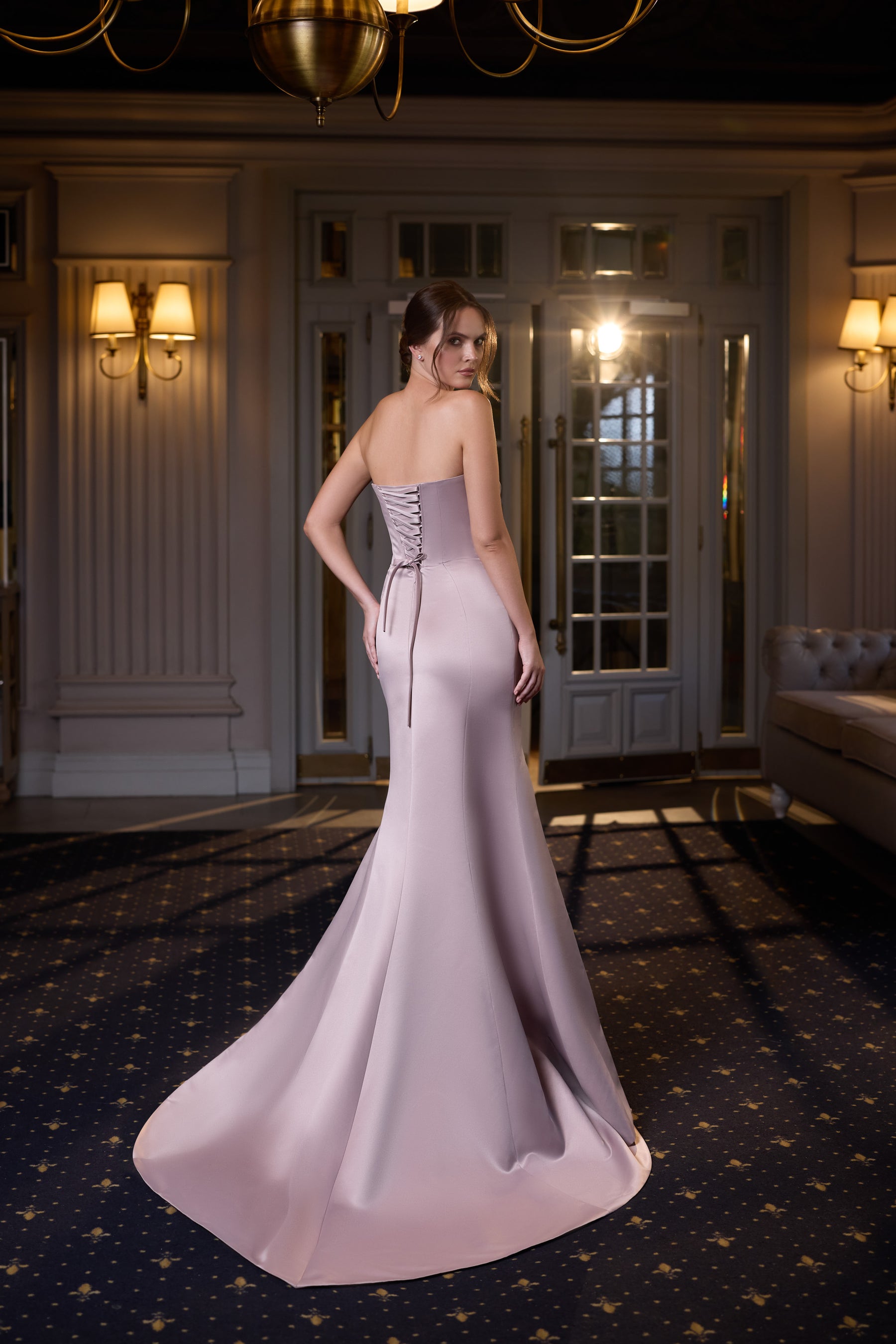 Back of a pale pink evening dress with a lace-up corset panel, strapless neckline, and sweeping train