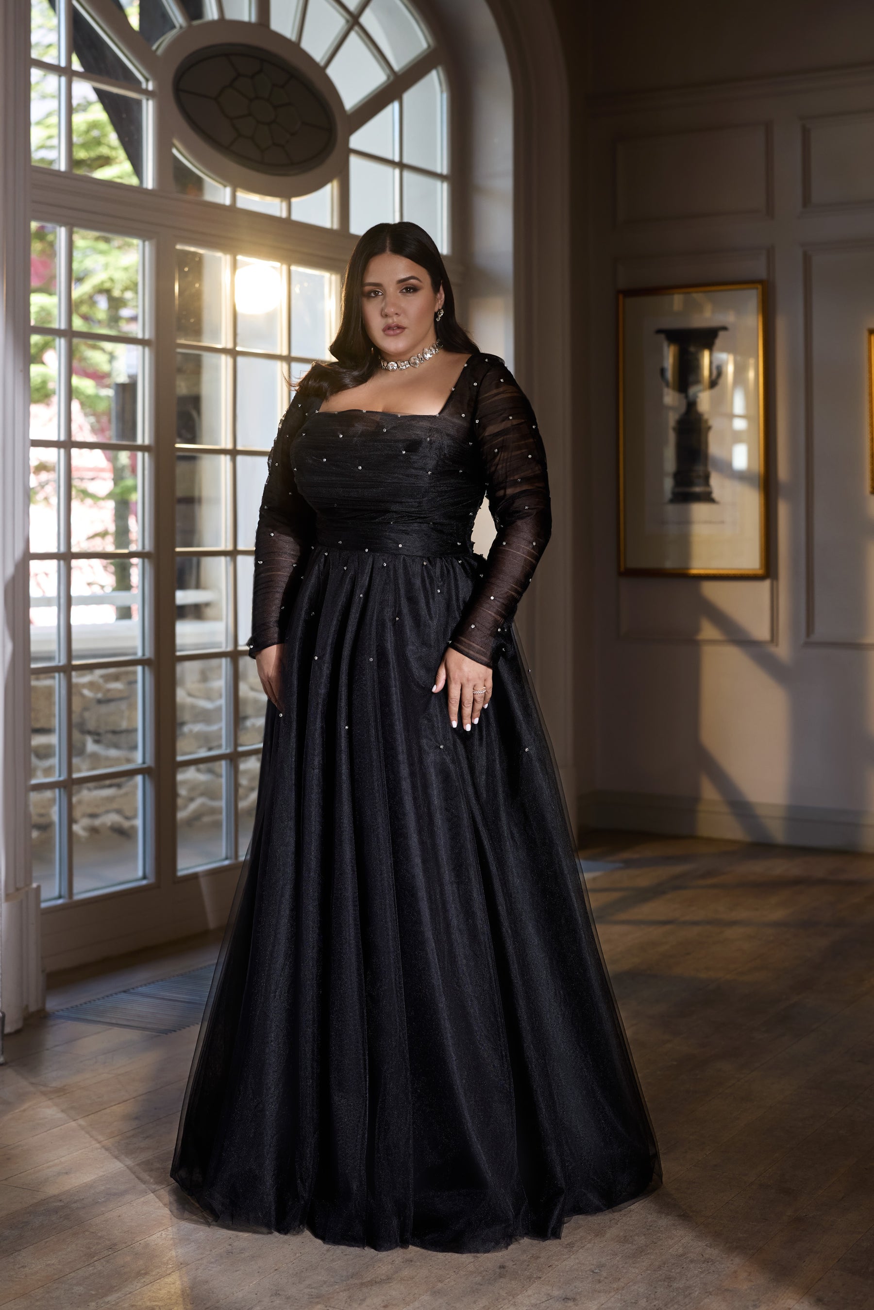 Black evening dress with a square neckline, sheer long sleeves, sparkling details, and a full floor-length skirt