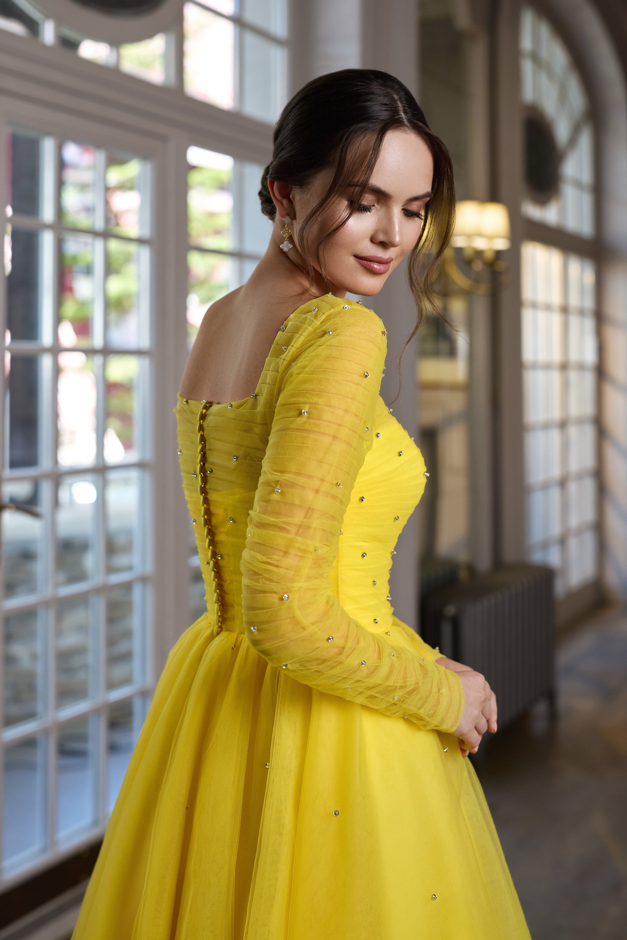 Yellow evening dress showing a square back with lace-up detailing, sheer embellished sleeves, and a full skirt