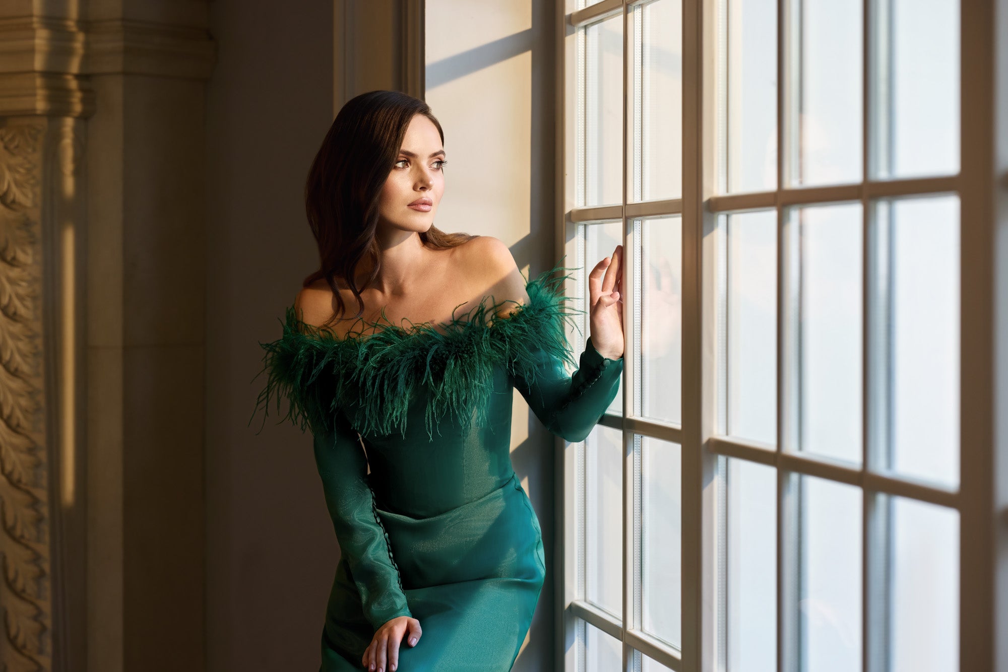 Fitted emerald green evening dress featuring long sleeves, an off-the-shoulder neckline, and feather trim