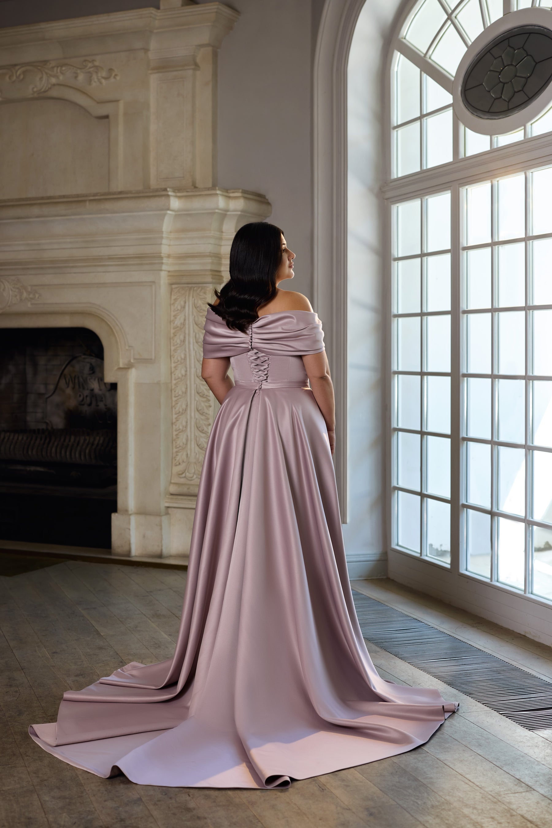 Mauve evening dress shown from behind with a draped off-shoulder neckline and flowing train