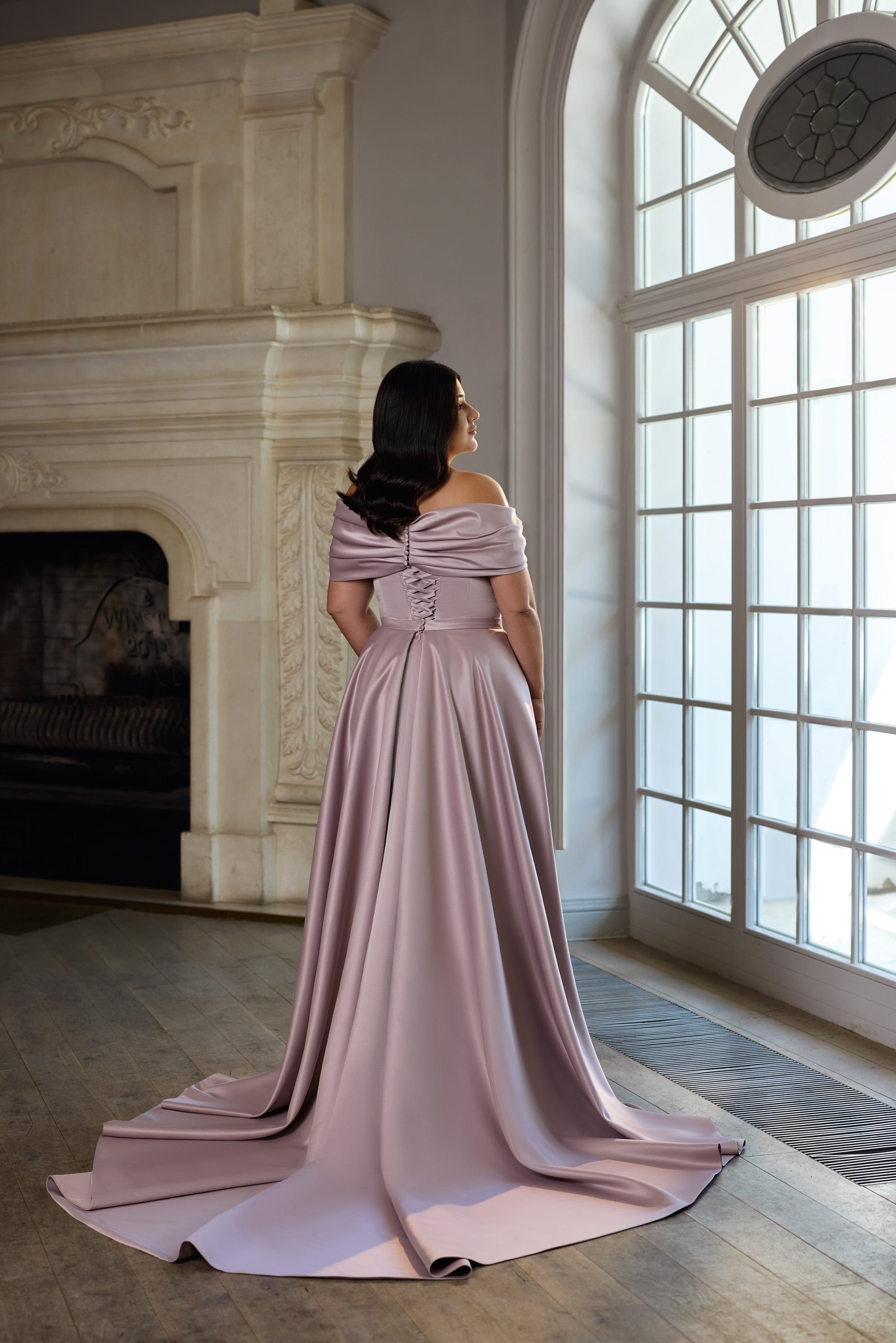 Mauve evening dress shown from behind with a draped off-shoulder neckline and flowing train
