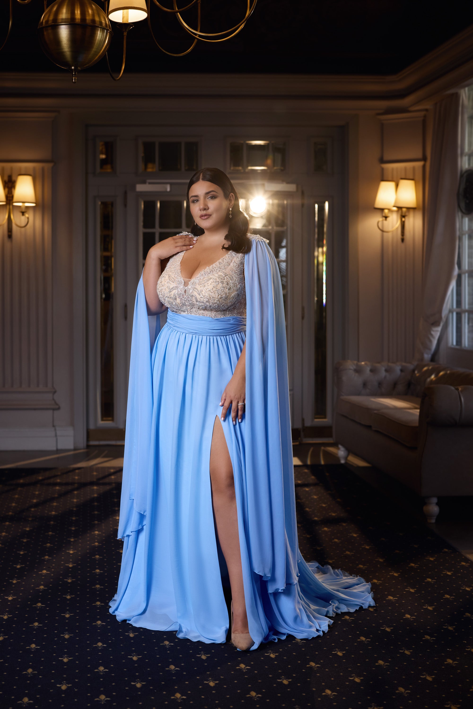 Light blue evening dress with a jeweled bodice, draped cape sleeves, flowing skirt, and high thigh slit
