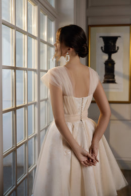 Back of an ivory evening dress with sheer sleeves, a low square back, and a row of buttons