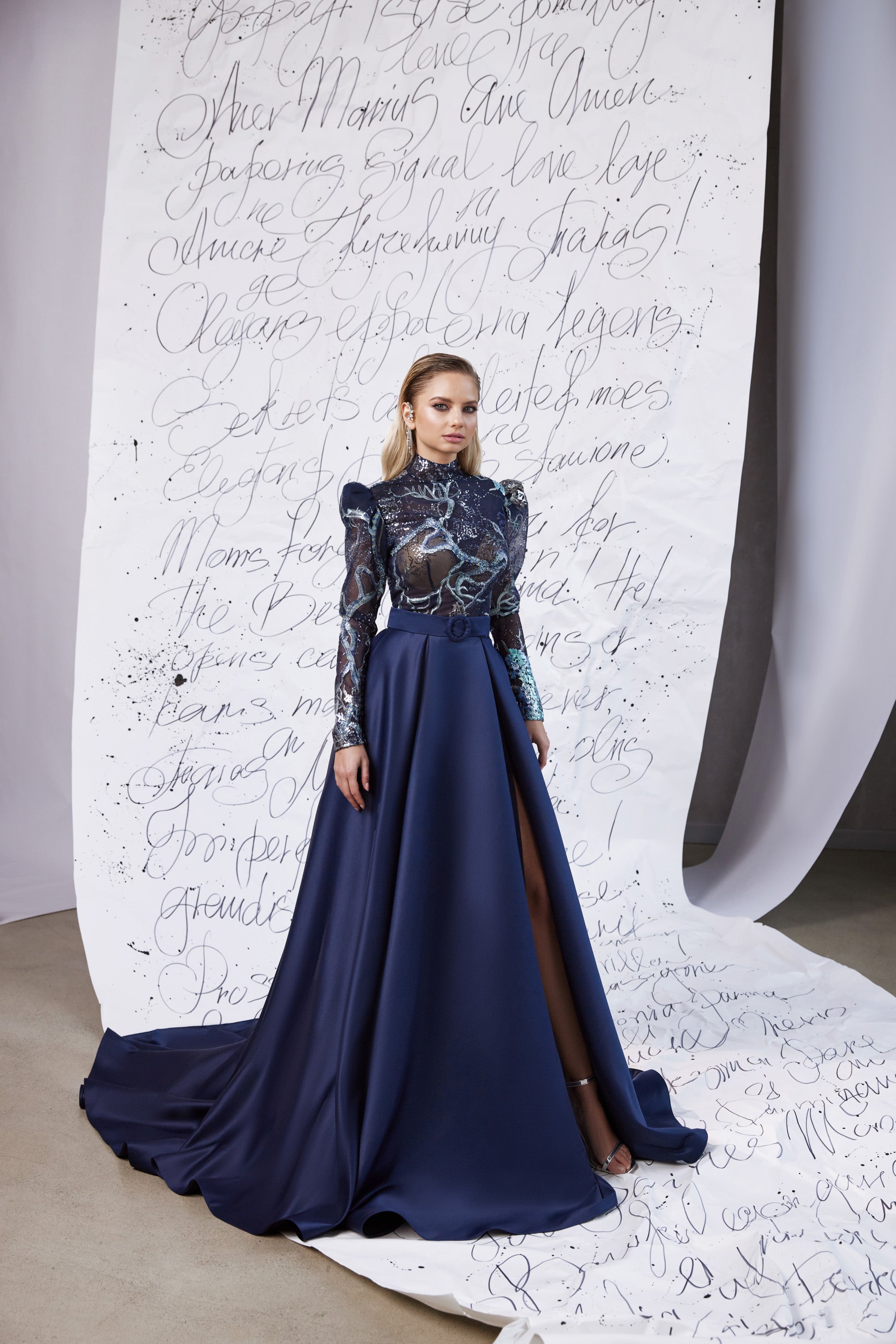 Navy evening dress with a high neckline, embellished long sleeves, flowing skirt, and thigh-high slit
