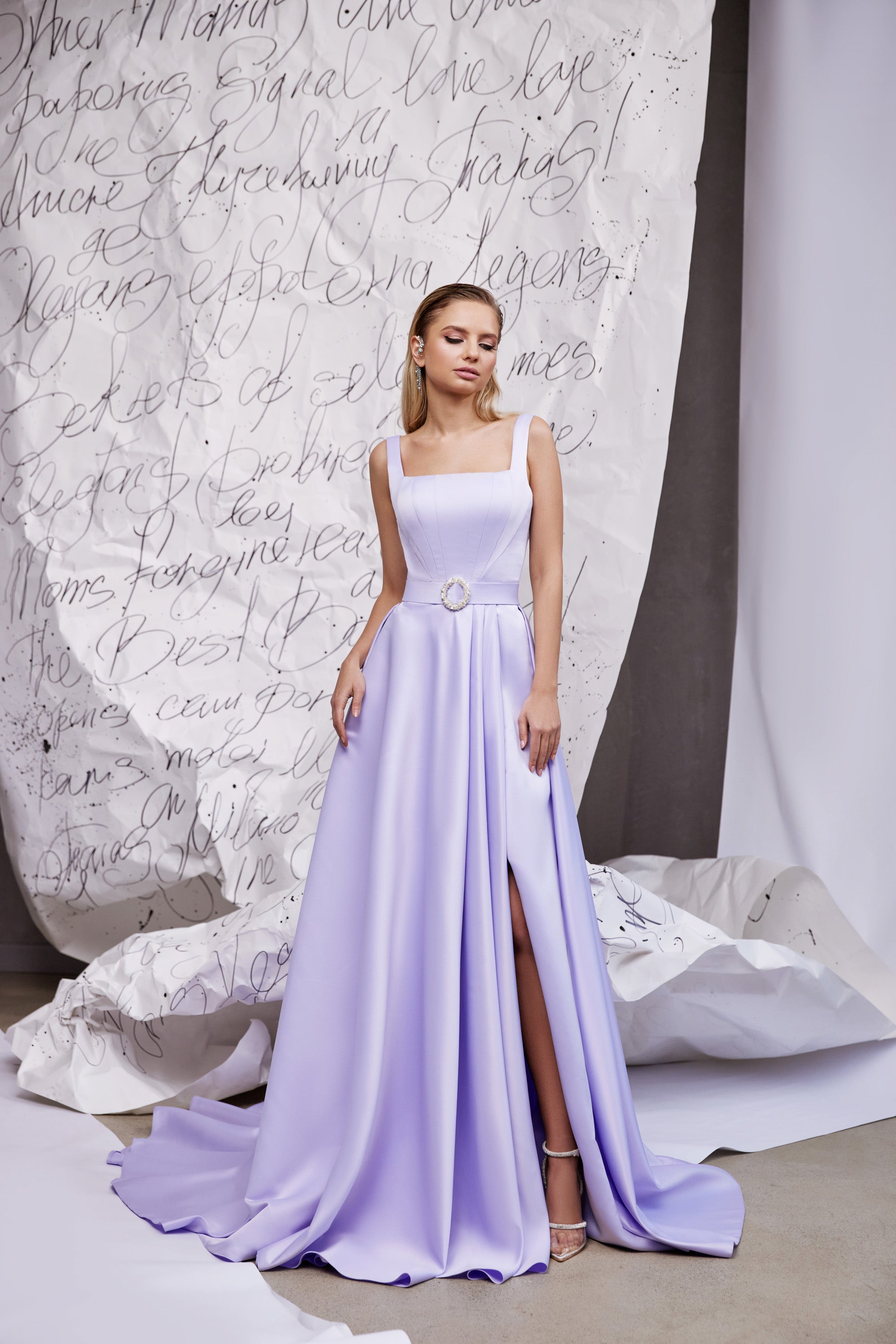 Full-length lavender evening dress with square neckline, thin straps, circular waist buckle, slit, and train