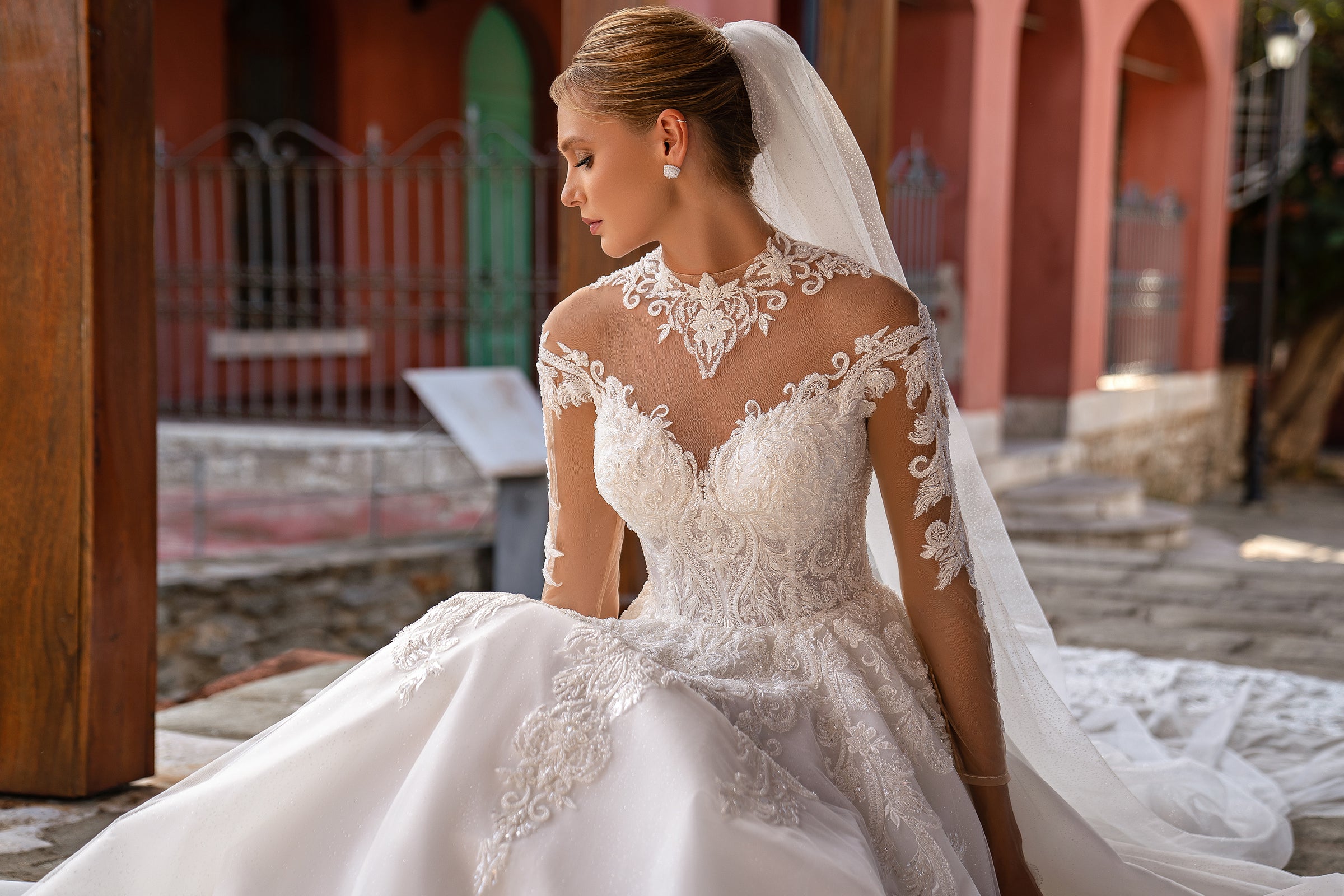 Dotted tulle wedding veil flowing behind the seated gown, with its sheer train visible on the ground