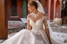 Dotted tulle wedding veil flowing behind the seated gown, with its sheer train visible on the ground