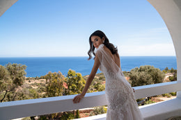 Open-back ivory wedding dress with lace detailing, sheer draped straps, and a fitted mermaid silhouette