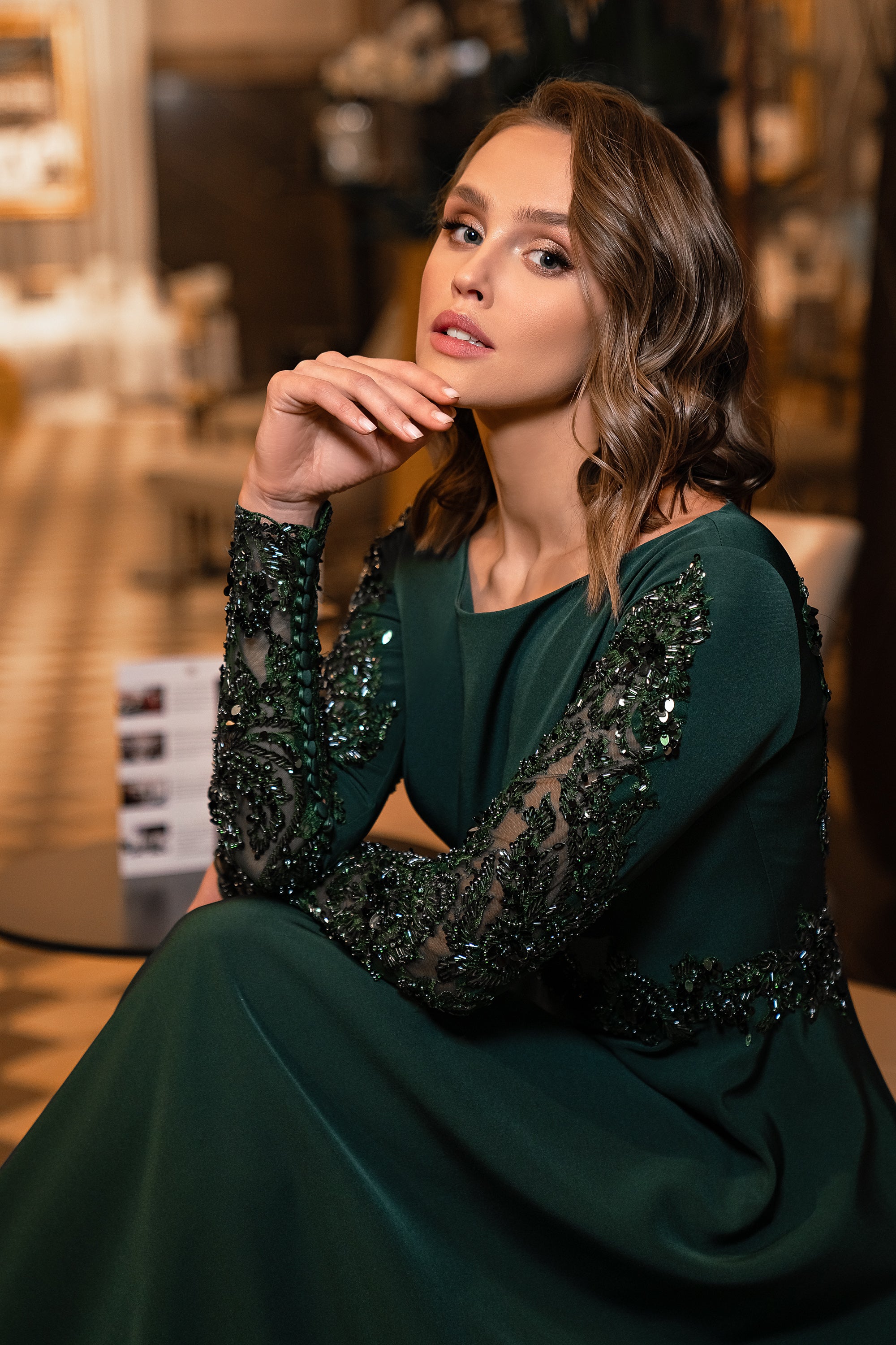 Close-up of an emerald evening dress with sheer sequined sleeves and ornate beadwork at the waist