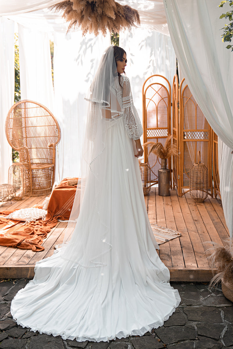 Open-back ivory wedding dress with floral lace sleeves, a flowing skirt, and a long train with lace appliqués