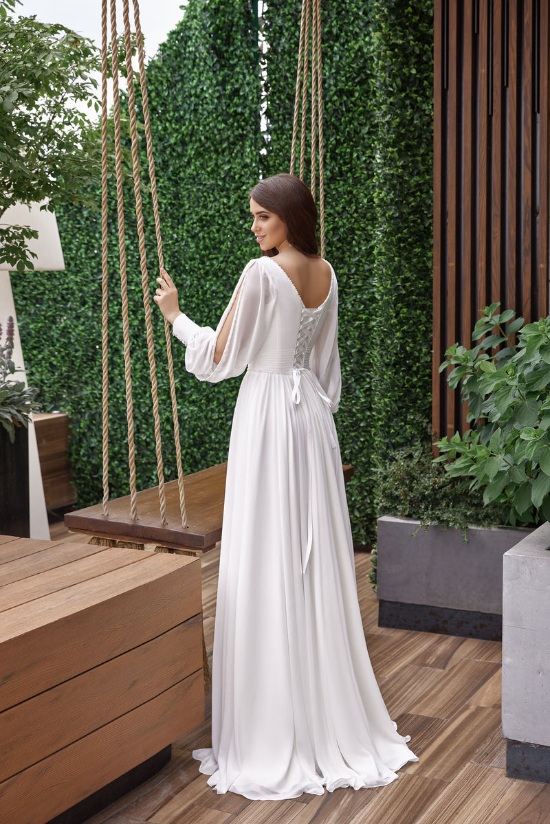 White wedding dress with an open V-back, bishop sleeves, tied waist, and softly draped floor-length skirt