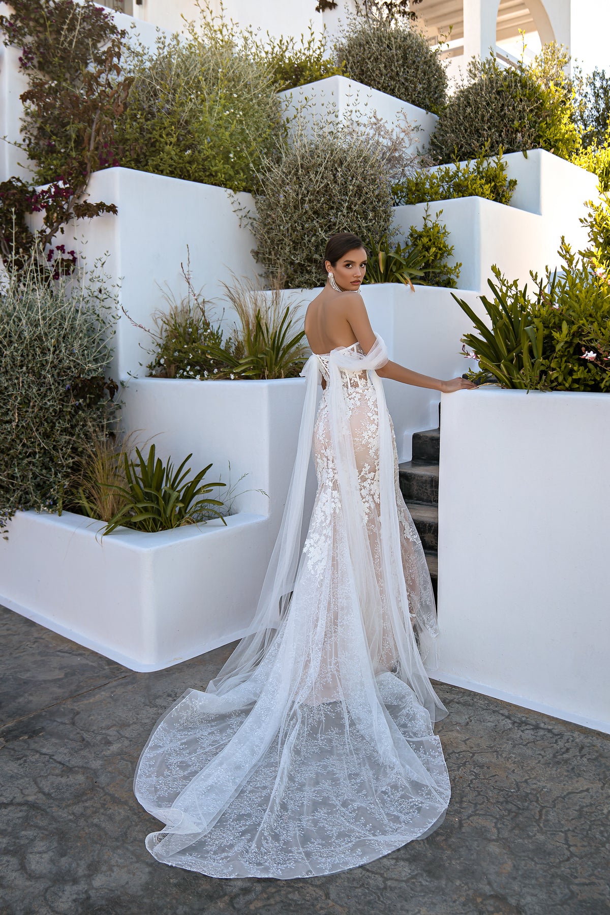 Open-back ivory wedding dress with floral lace panels, draped sleeves, and a long scalloped train