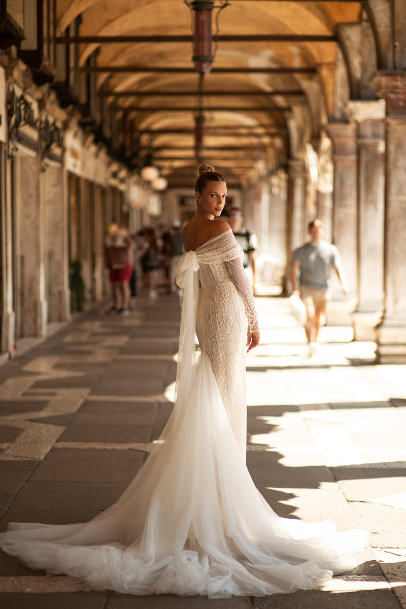 Angled back view of an ivory wedding dress with a large tulle bow and sweeping detachable train