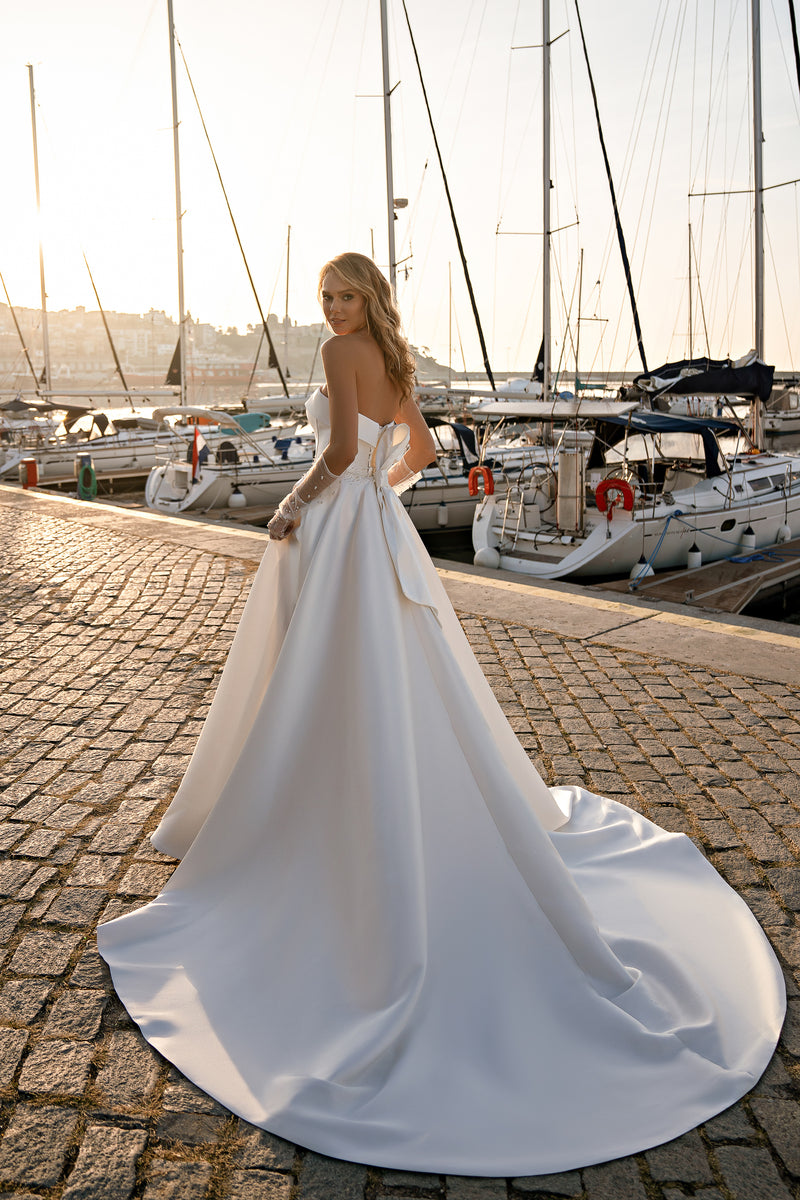 White wedding dress with an open strapless back, fitted waist, full skirt, and long trailing train