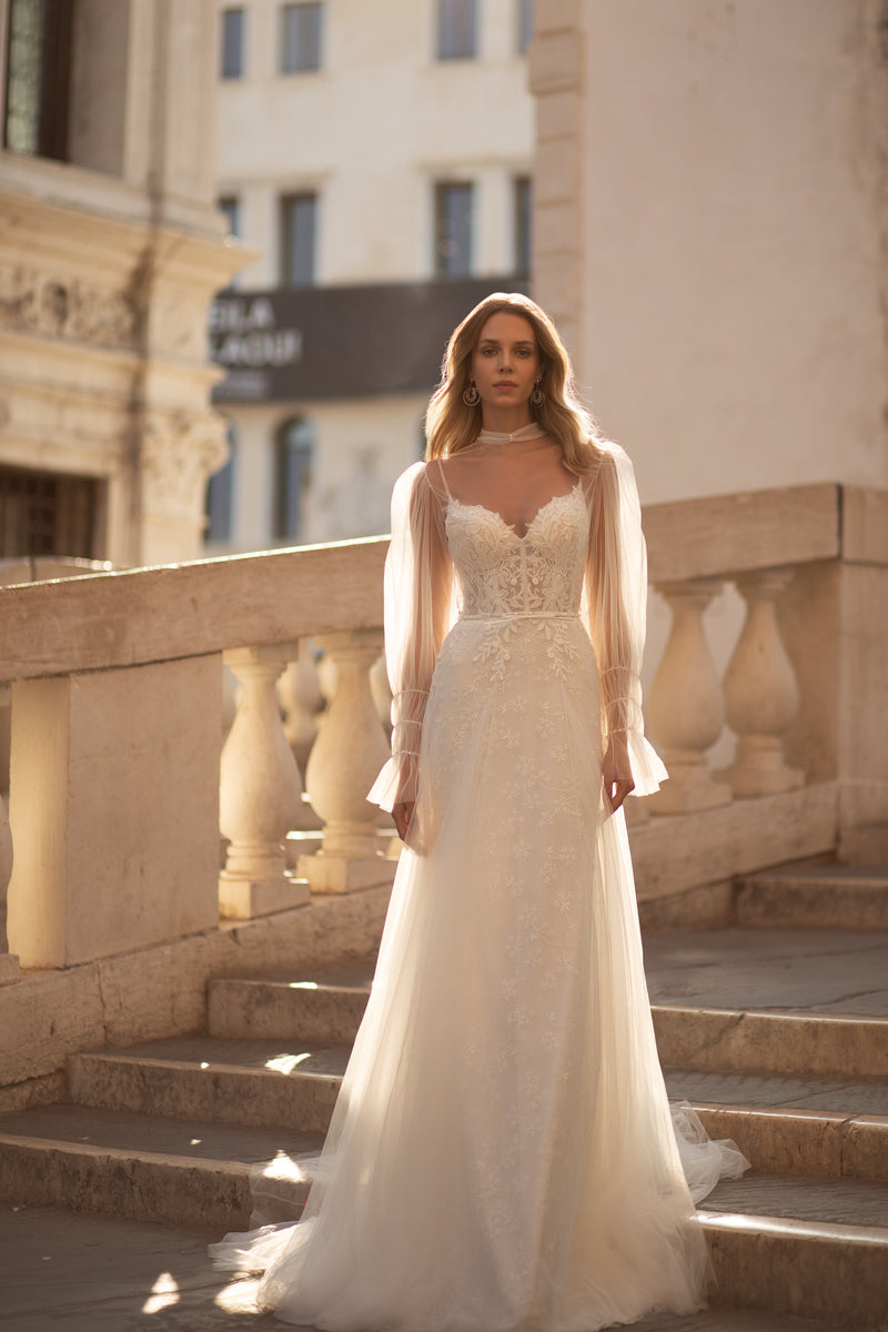 Ivory flared wedding dress with floral lace bodice, sheer long sleeves, and a flowing train