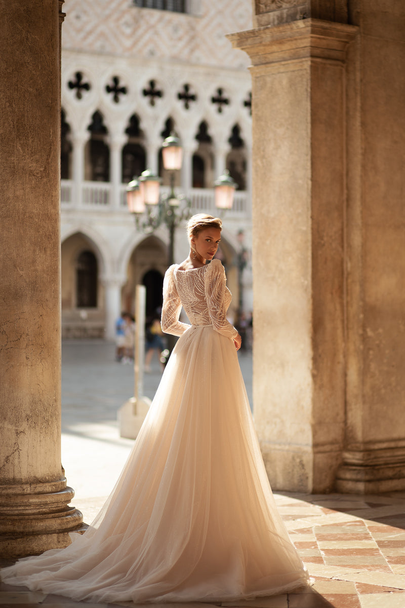 Long-sleeved ivory wedding dress with a sparkling patterned bodice and full flowing skirt with a train