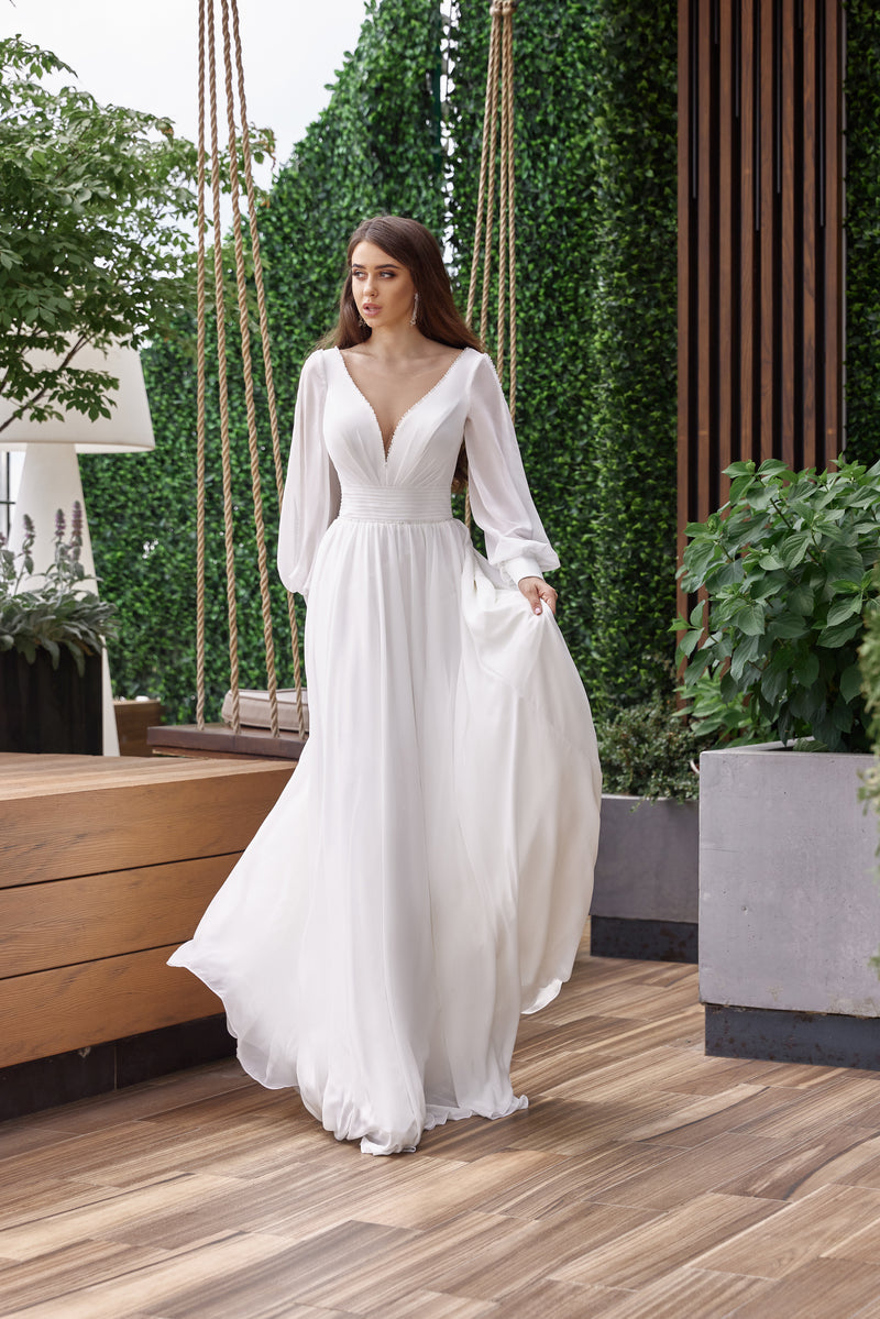 White A-line wedding dress with a deep V-neckline, bishop sleeves, gathered waist, and flowing skirt