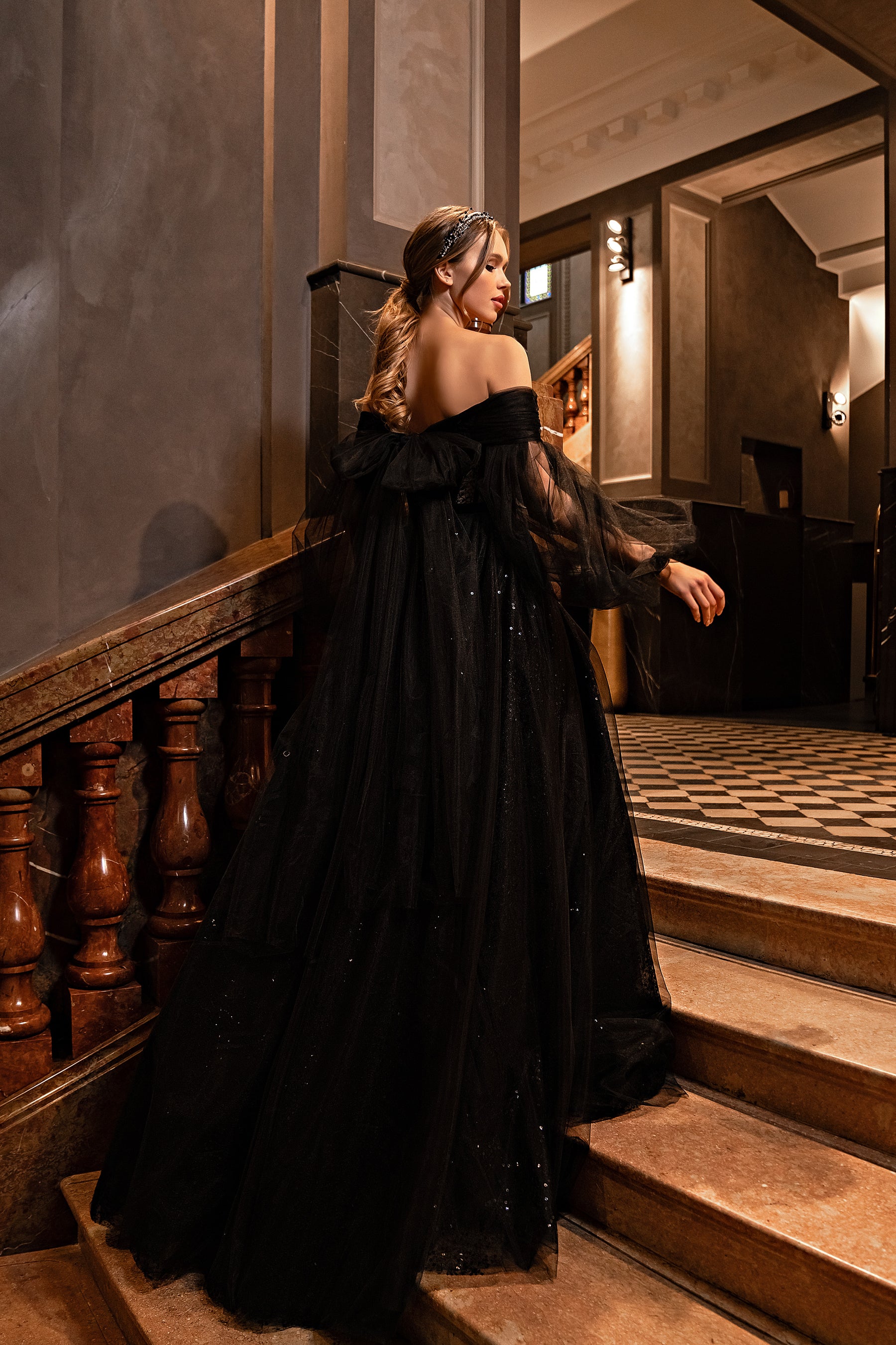 Black evening dress shown from the back with an off-the-shoulder neckline and full trailing skirt