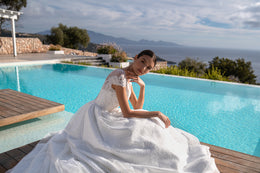 Seated white wedding dress showing short lace sleeves, a sparkling bodice, and a voluminous skirt