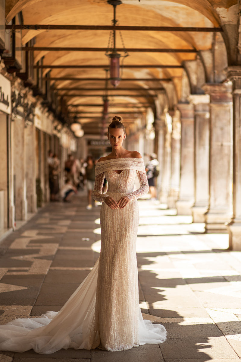 Ivory beaded sheath wedding dress with an off-the-shoulder neckline, long sleeves, and flowing tulle train
