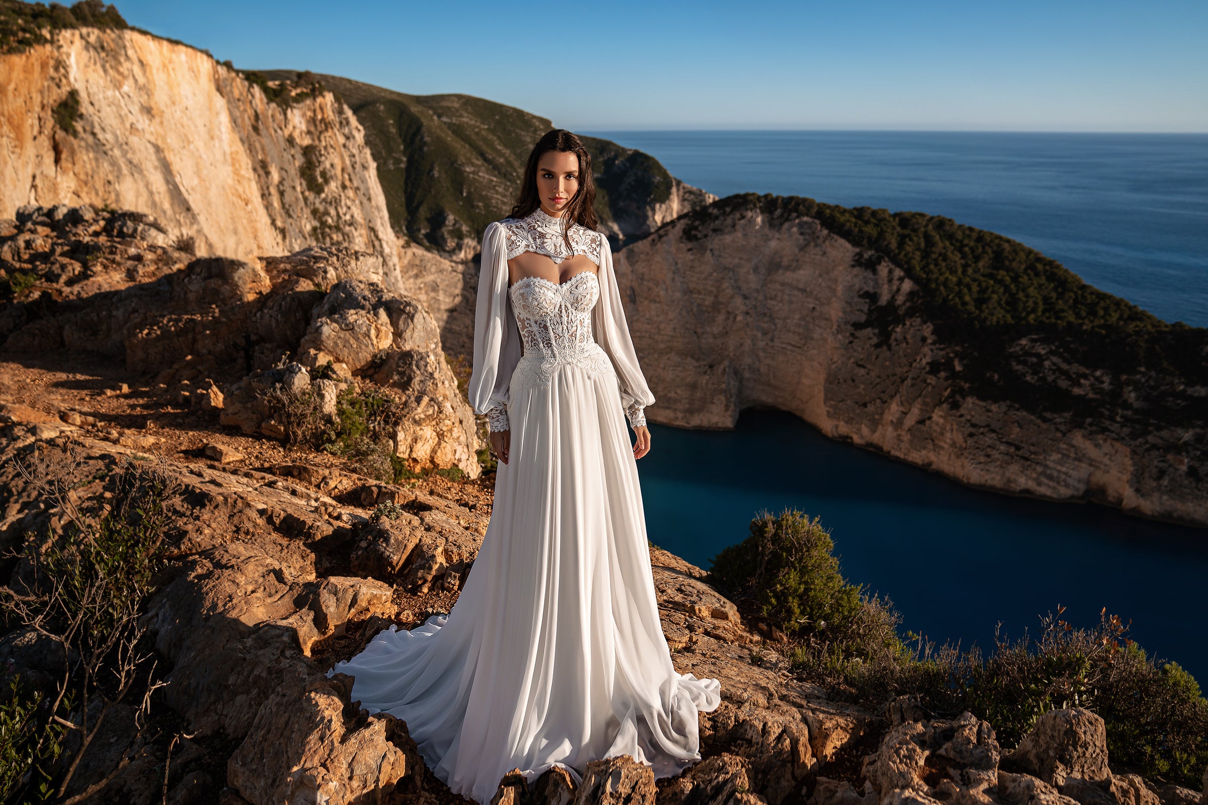 Full-length ivory wedding dress with a lace bodice, high neckline, sheer long sleeves, and extended train