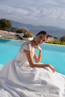 Seated white wedding dress showing its sparkling lace bodice, illusion neckline, and full gathered skirt