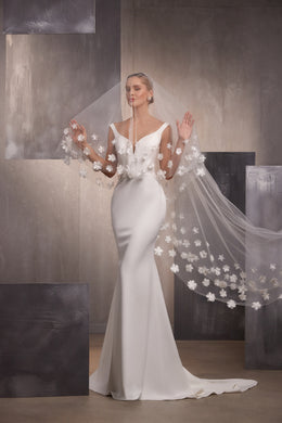 Sheer wedding veil with voluminous white floral embroidery and sparkling accents cascading beside a fitted gown