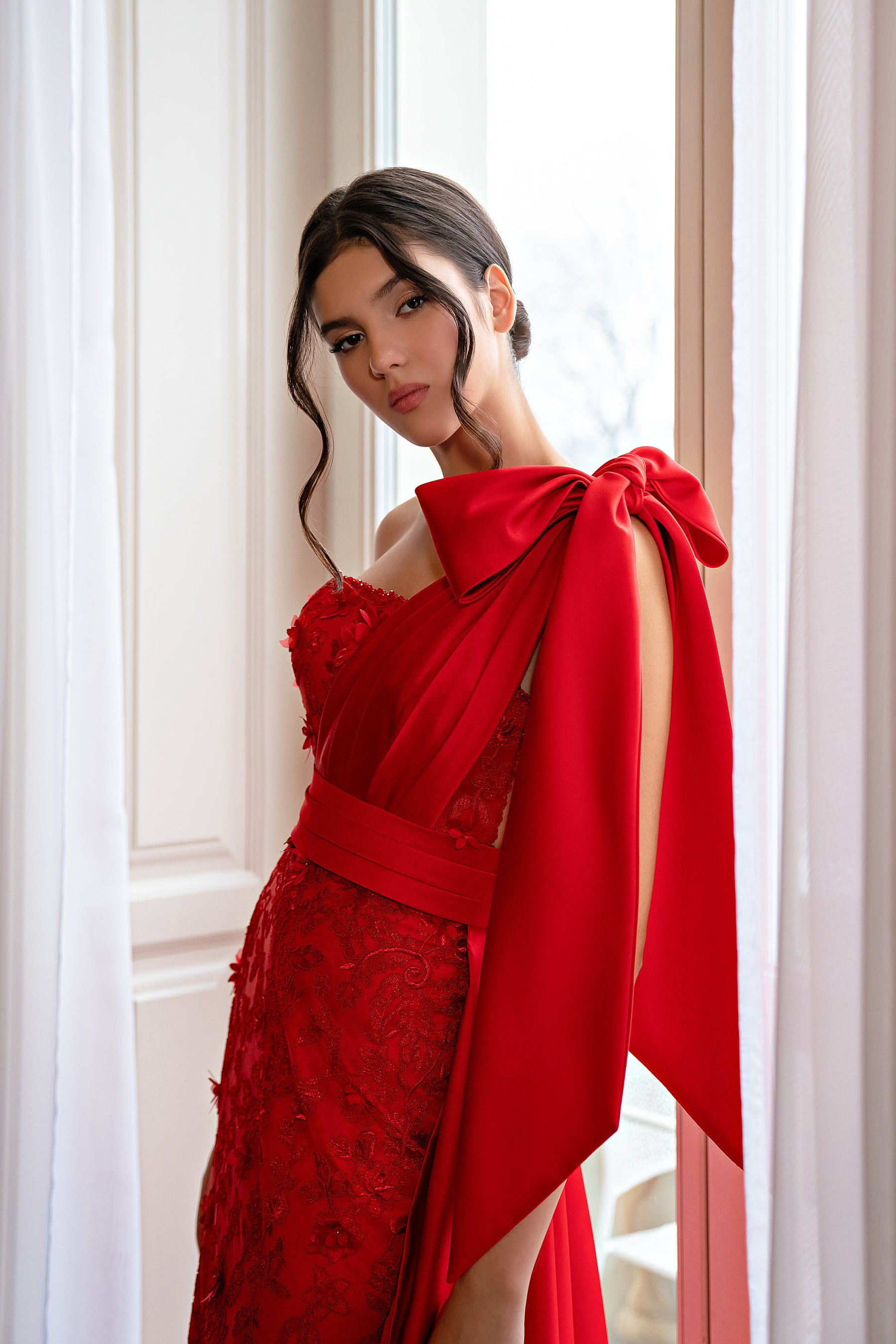 Close-up of a red lace evening dress with a one-shoulder neckline and oversized bow drape