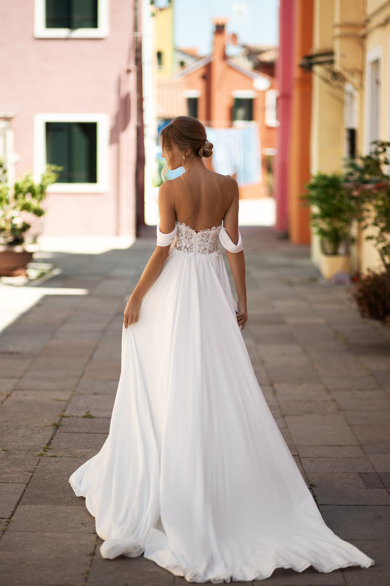 Open-back ivory wedding dress with a lace waist, off-shoulder sleeves, flowing skirt, and long train