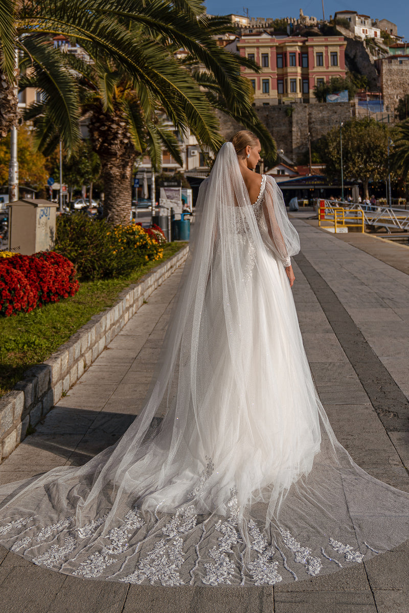 Back of an ivory wedding dress showing a low V-shaped lace back, sheer sleeves, and a long embellished train